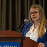 Another speaks shares remarks at the podium wearing a blue blazer